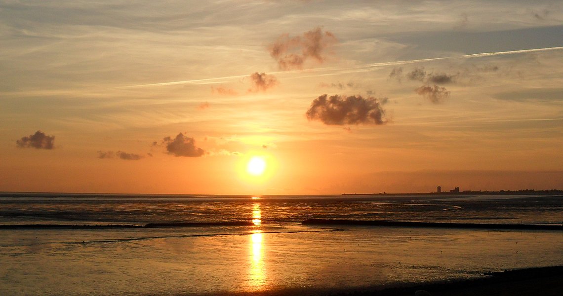 Blick über die Nordsee bei Ebbe Richtung Büsum beim Sonnenuntergang. Das Wattenmeer reflektiert die Sonnenstrahlen