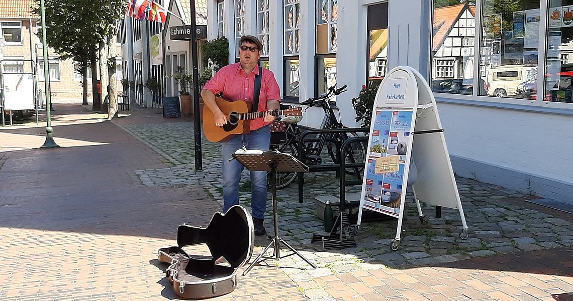 Henning Gumann spielt auf seiner Gitarre bei strahlendem Sonnenschein vor der Touristinfo