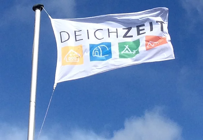 eine weiße Flagge mit dem Schriftzug DEICHZEIT flattert vor blauem Himmel